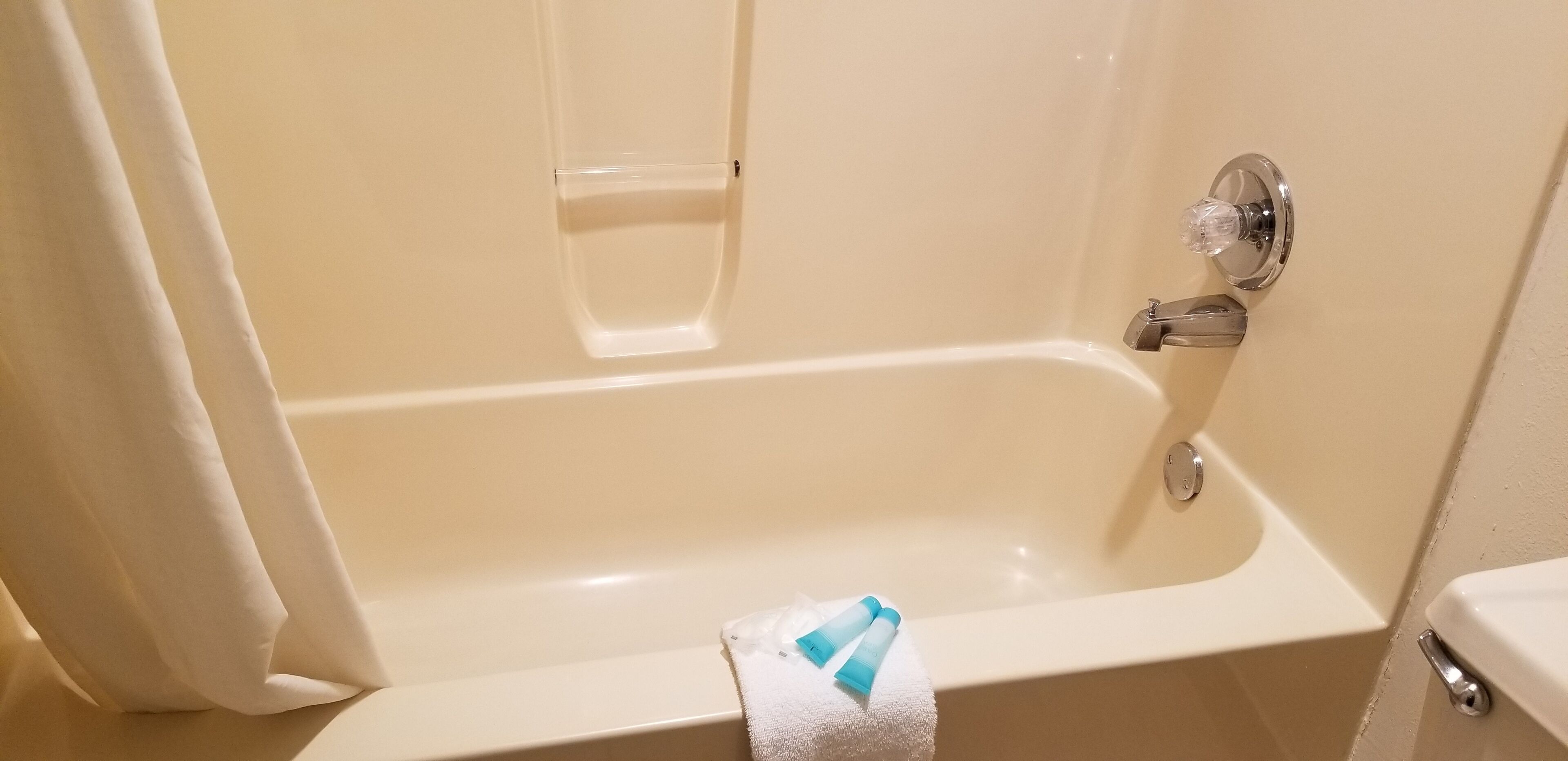 A bathtub with a white towel and two blue bottles on it.