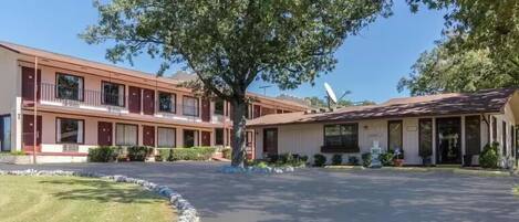 Un motel con un césped central, un árbol grande y un edificio de fachada roja y numerosas ventanas.