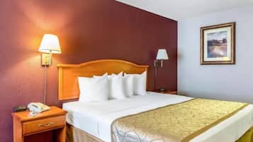 A hotel room with a wooden headboard, a white bedspread, a yellow accent bedspread, a bedside lamp, a nightstand with a phone, and a framed picture on the wall.
