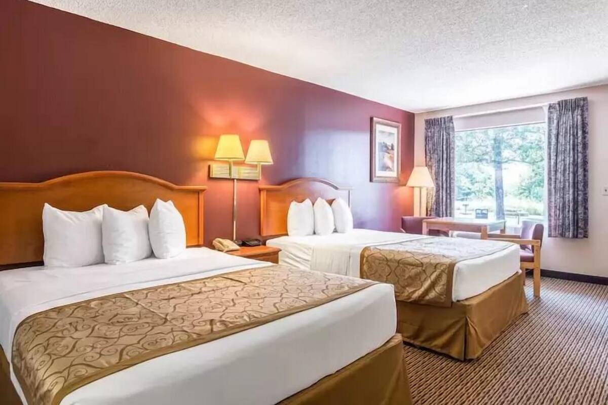 A hotel room with two beds, a desk, a chair, and a window with curtains.