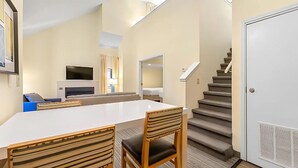 A hotel room with a dining area, a sofa, a TV, and a staircase. - Sonesta ES Suites Cincinnati - Sharonville West (Sharonville)