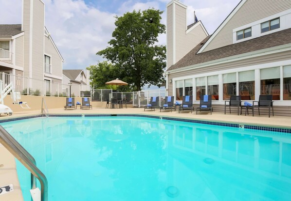 Relax by the pool surrounded by lounge chairs and umbrellas, with a tree providing a natural backdrop.