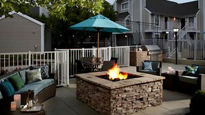 An outdoor patio with a stone fire pit, a white fence, and a blue umbrella. - Sonesta ES Suites Cincinnati - Sharonville West (Sharonville)