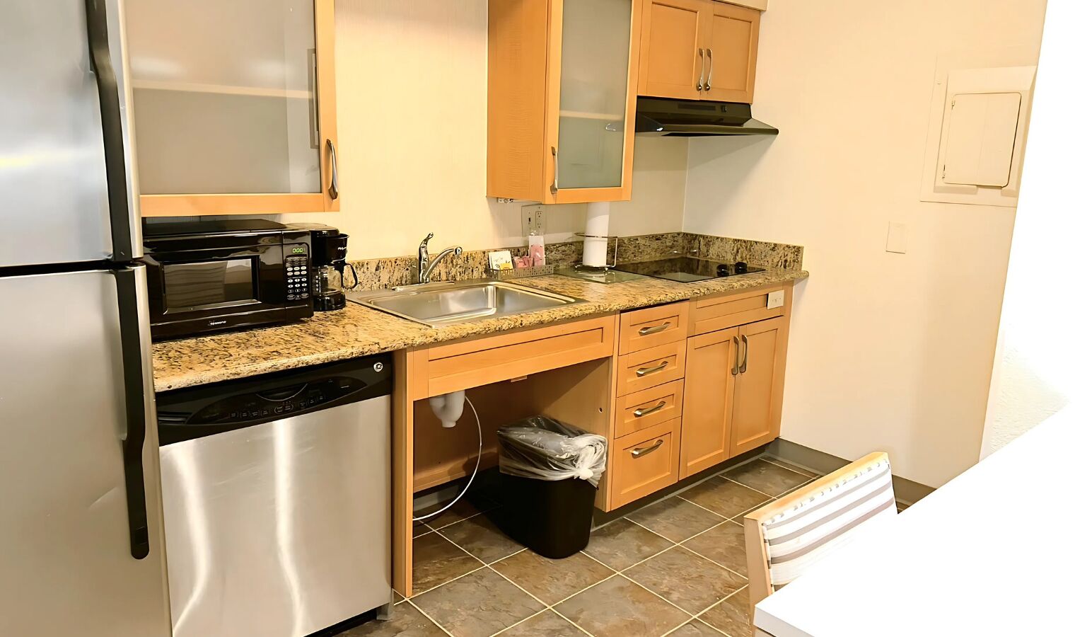 A compact kitchen with a refrigerator, microwave, coffee maker, sink, and wooden cabinets.