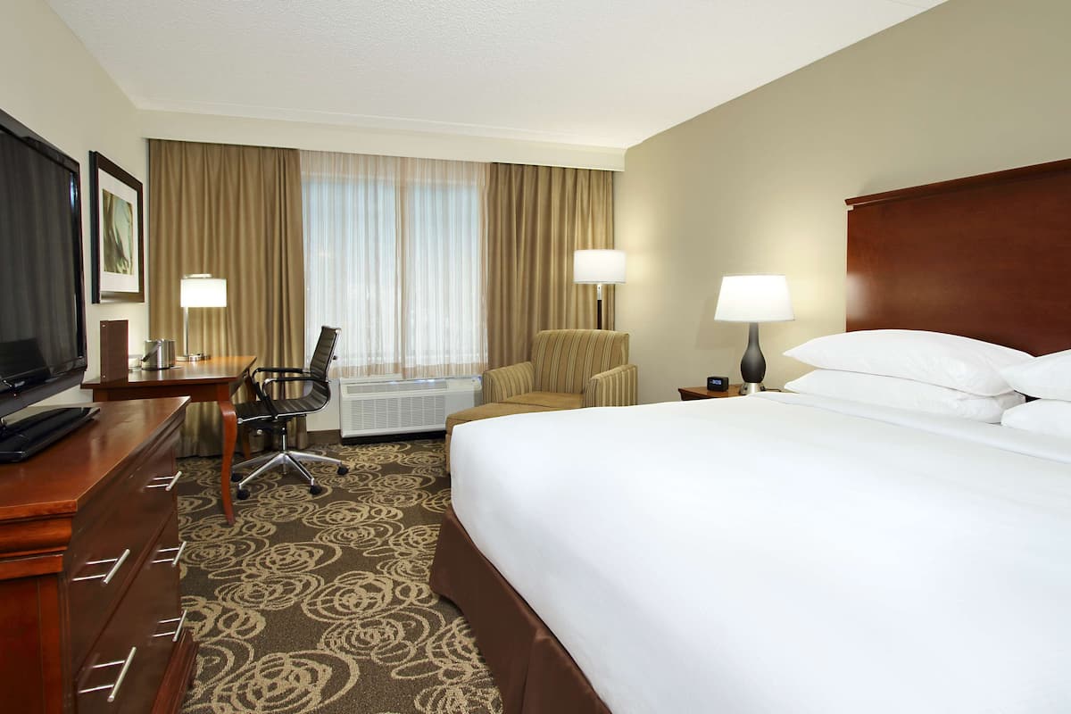 A hotel room with a large bed, a desk with a chair, a lamp, and a window with curtains.