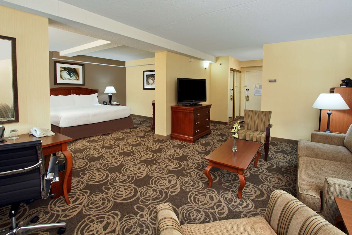 A hotel room with a bed, a television, a desk with a lamp, a chair, and a sofa.