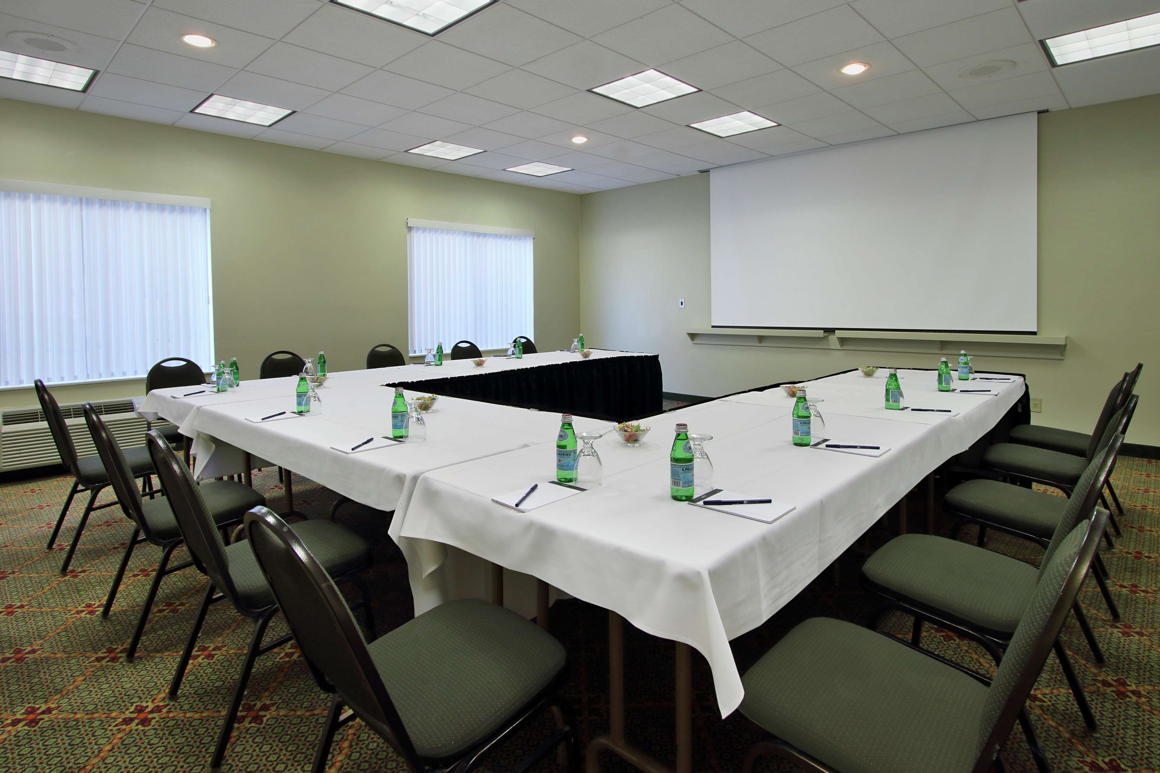 A conference room with a long table, chairs, water bottles, and a projector screen.