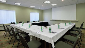 A conference room with a long table, chairs, water bottles, and a projector screen.