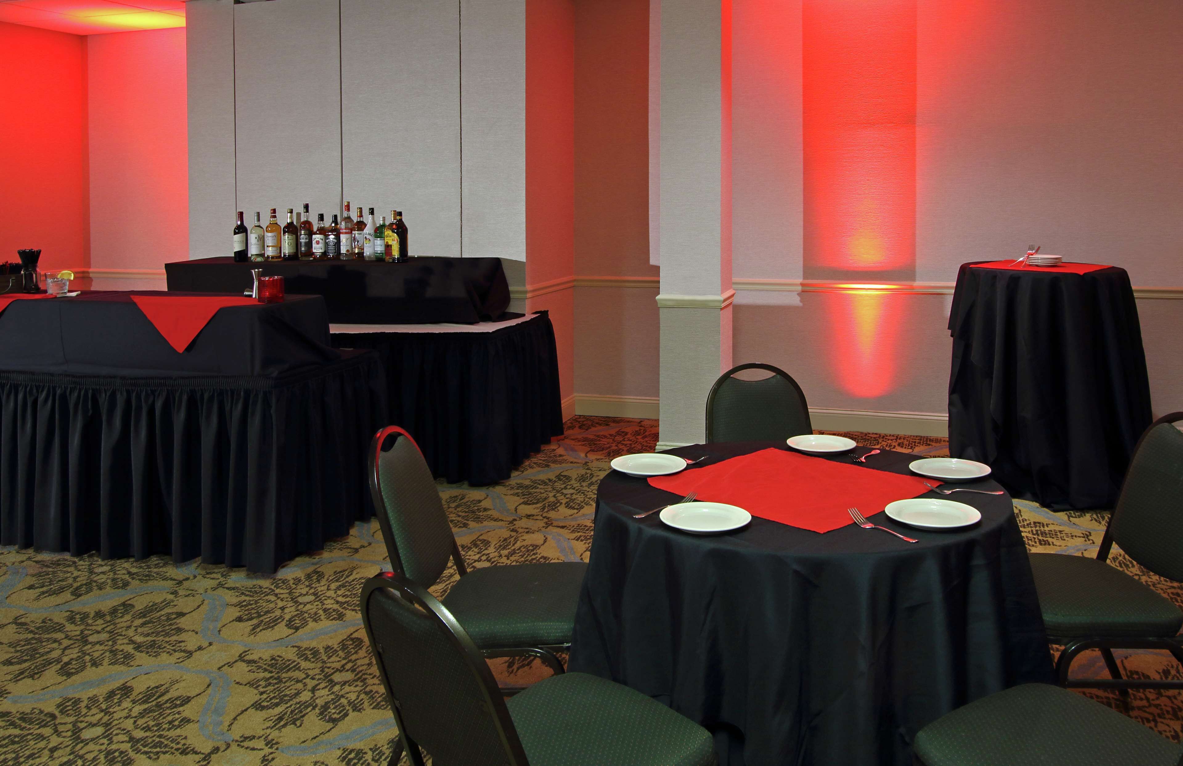 Een congrescentrum met ronde tafels, stoelen, een bar met flessen en een rode muur.