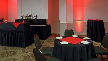 Een congrescentrum met ronde tafels, stoelen, een bar met flessen en een rode muur.