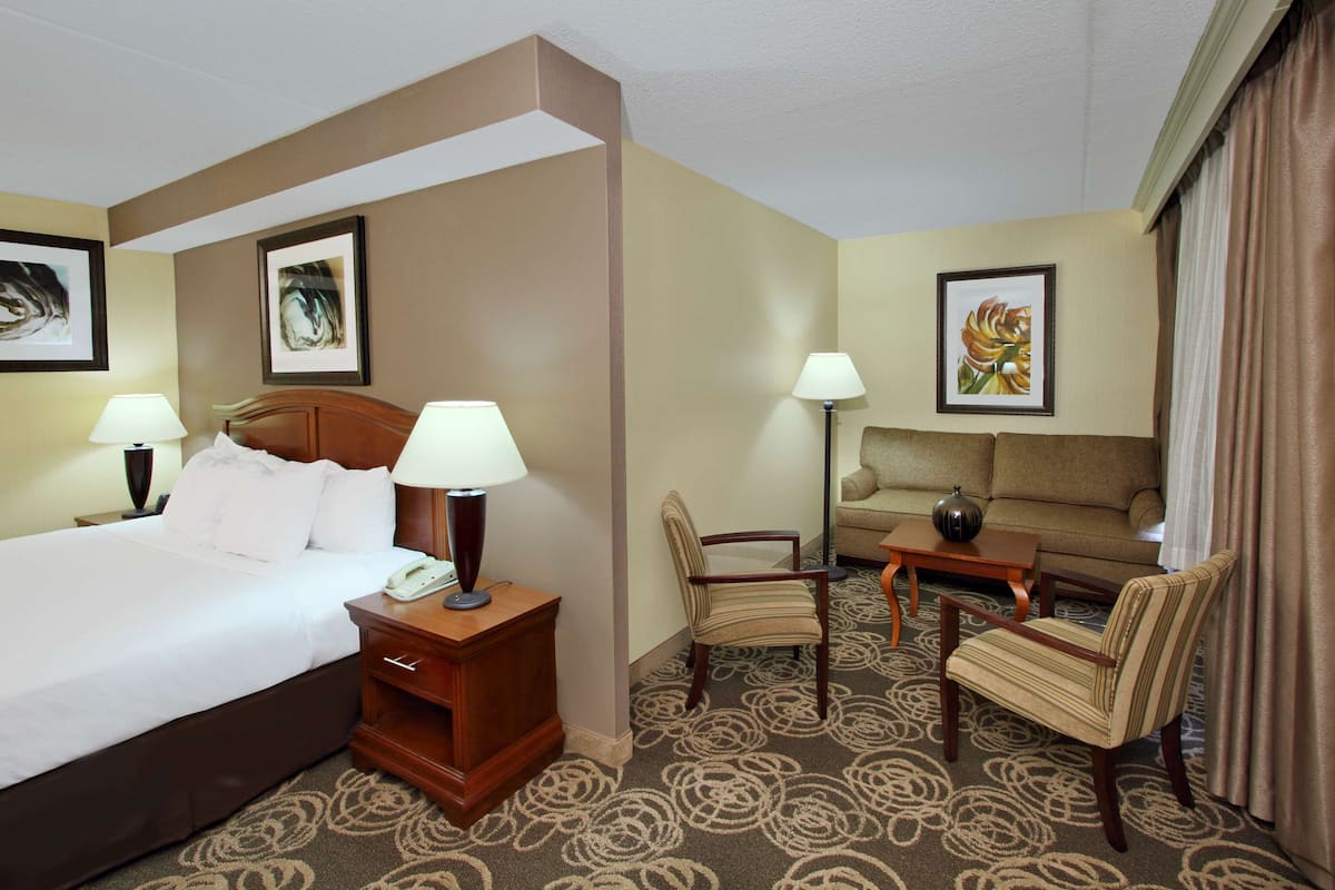A hotel room with a bed, two bedside tables with lamps, a sofa, two armchairs, and a coffee table.