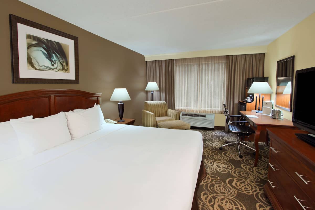 A hotel room with a large bed, two chairs, a desk with a television, and a coffee maker.