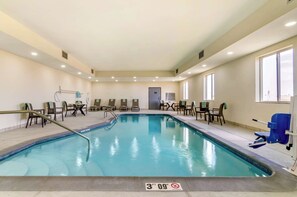 An indoor swimming pool with a 3 FT 9 IN depth marker, surrounded by lounge chairs and tables, with a door in the background.