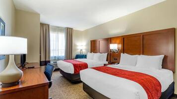 A hotel room with two beds, a desk with a lamp, a chair, and a window with curtains.