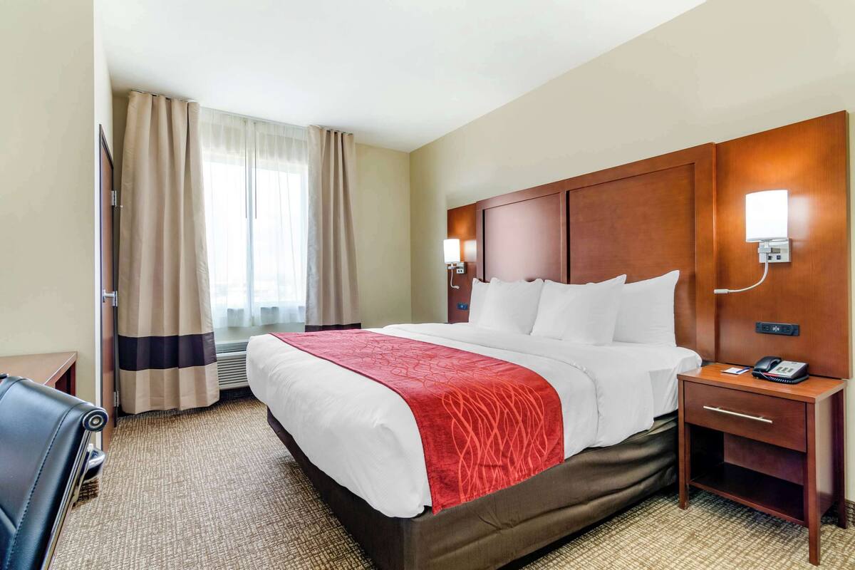A hotel room with a large bed, a wooden headboard, a bedside table with a phone, and a chair.