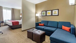 Quarto de hotel com uma cama, um sofá, um banquinho e uma luminária. Há quadros nas paredes.