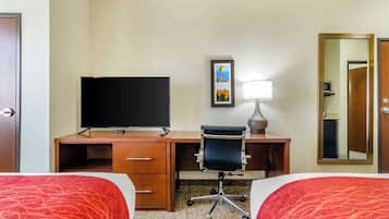 A hotel room with two beds, a desk with a TV, a chair, a lamp, and a framed picture on the wall.