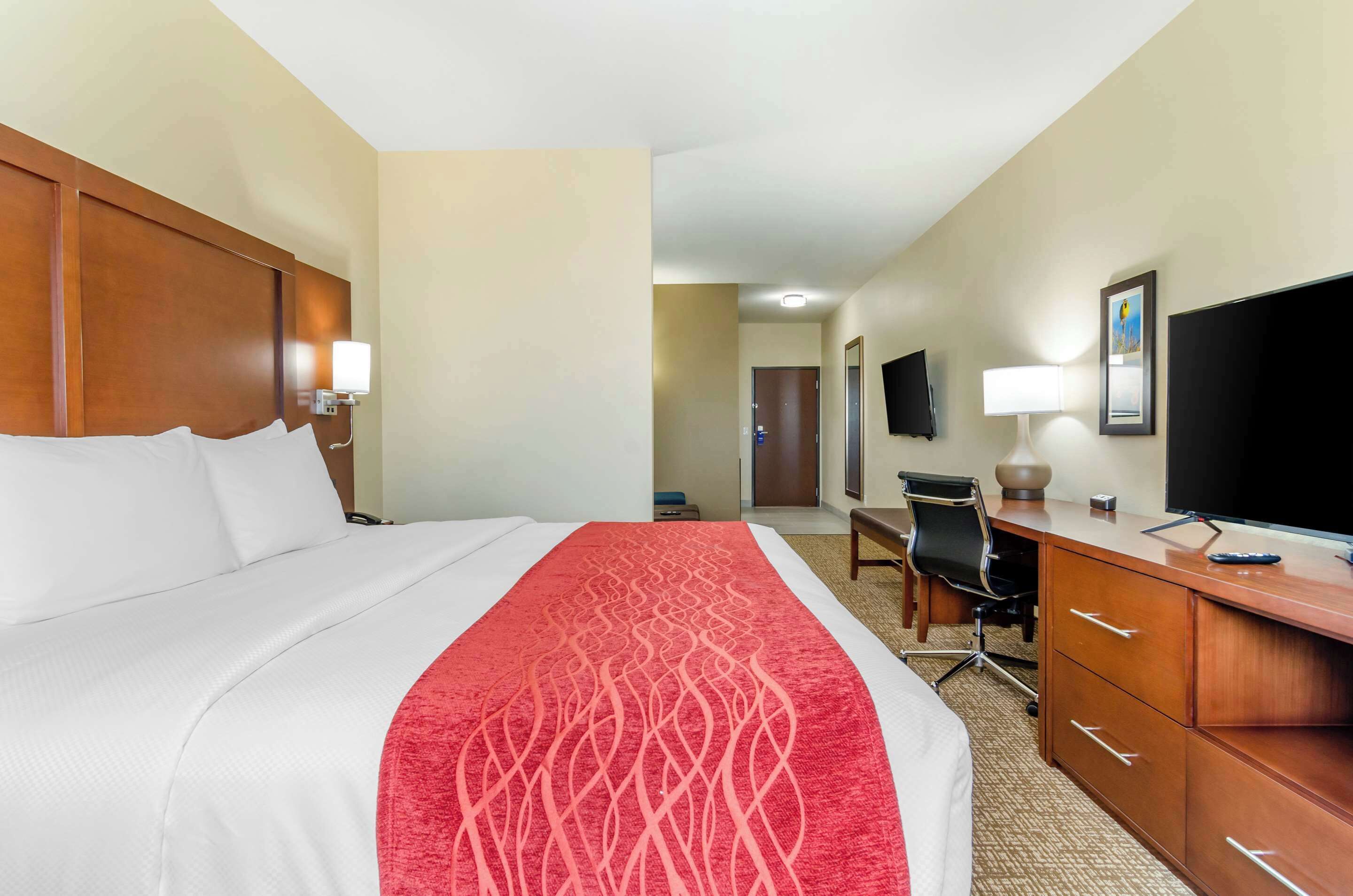 Habitación de hotel con una cama grande, un escritorio, una silla, un televisor y una puerta que da a otra habitación.