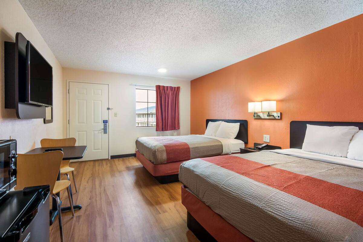 A hotel room with two beds, a desk, a chair, a TV, and a window with a view.
