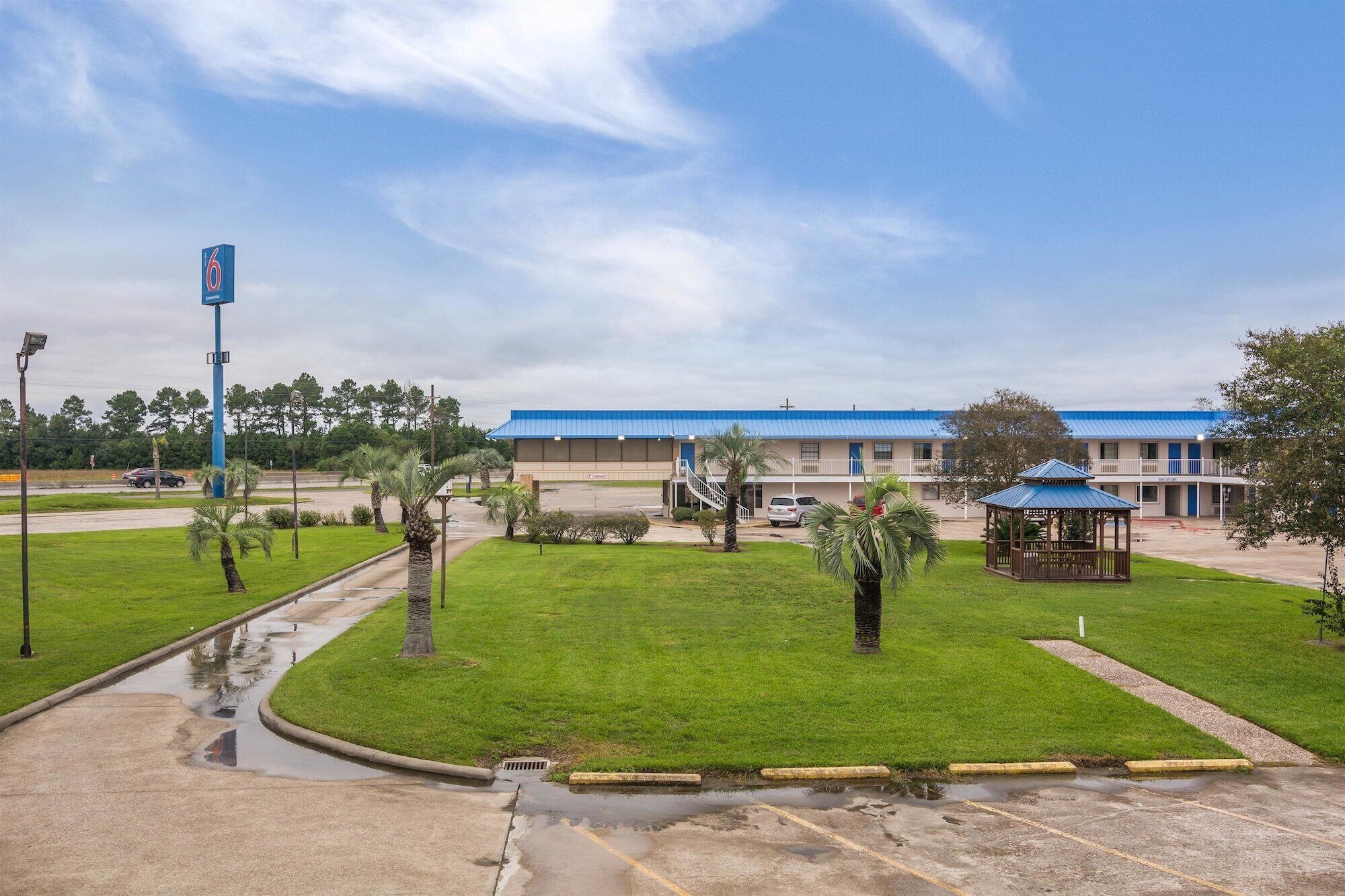A motel with a blue roof, a covered outdoor seating area, and a parking lot with visible puddles.
