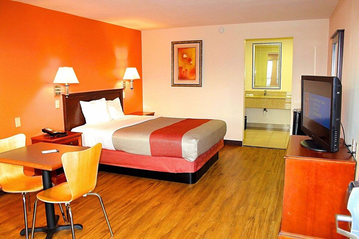 A hotel room with a bed, two bedside lamps, a desk with a chair, a television, and a bathroom visible through an open door.