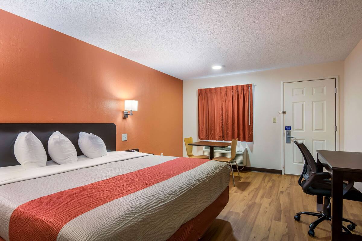 A hotel room with a bed, a desk, a chair, and a door.