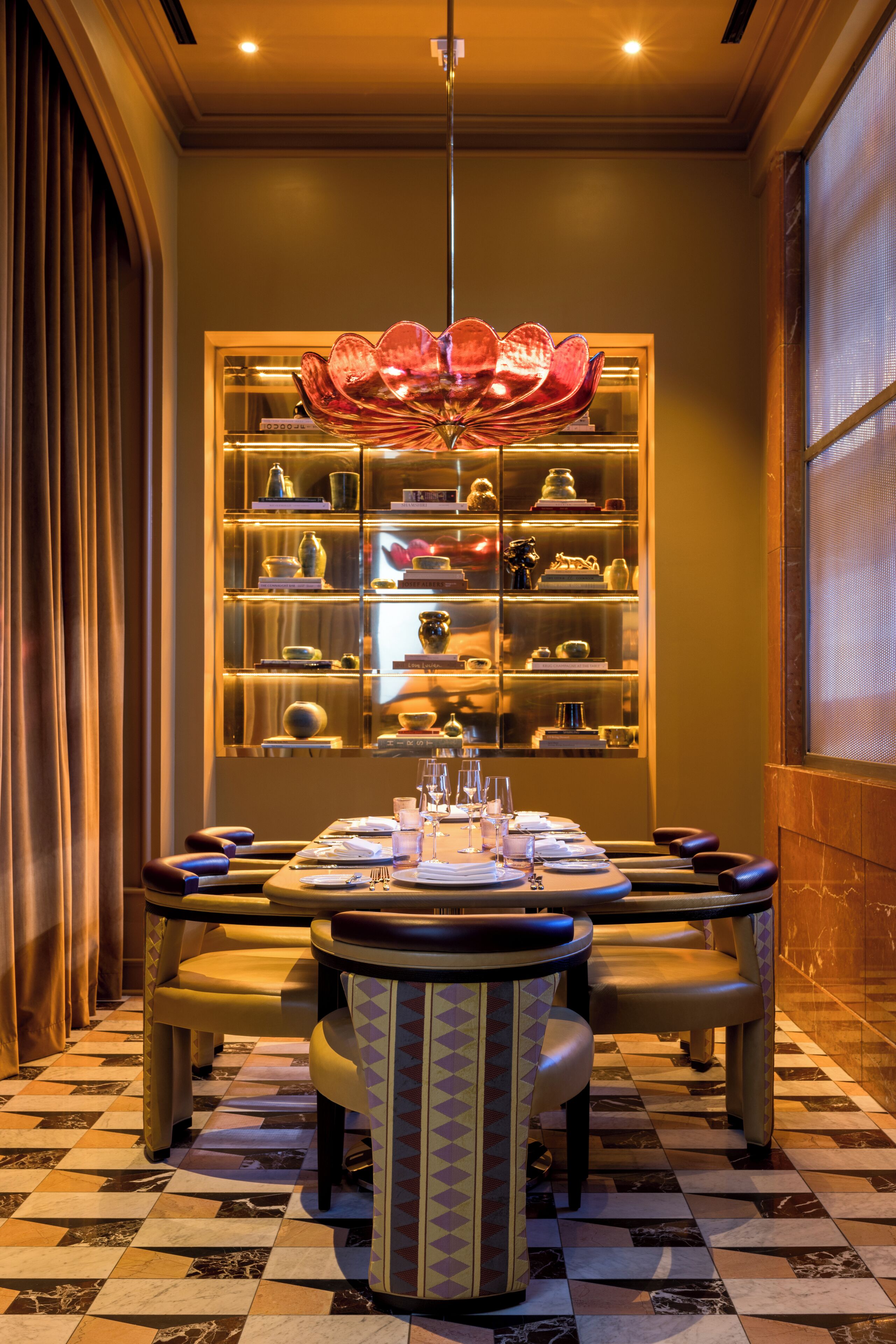 A dining area with a chandelier, a glass display case with decorative items, and a checkered floor.