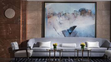 Een moderne lobby met een grijze bank, twee ronde tafels, een stoel en een groot abstract schilderij aan de muur.