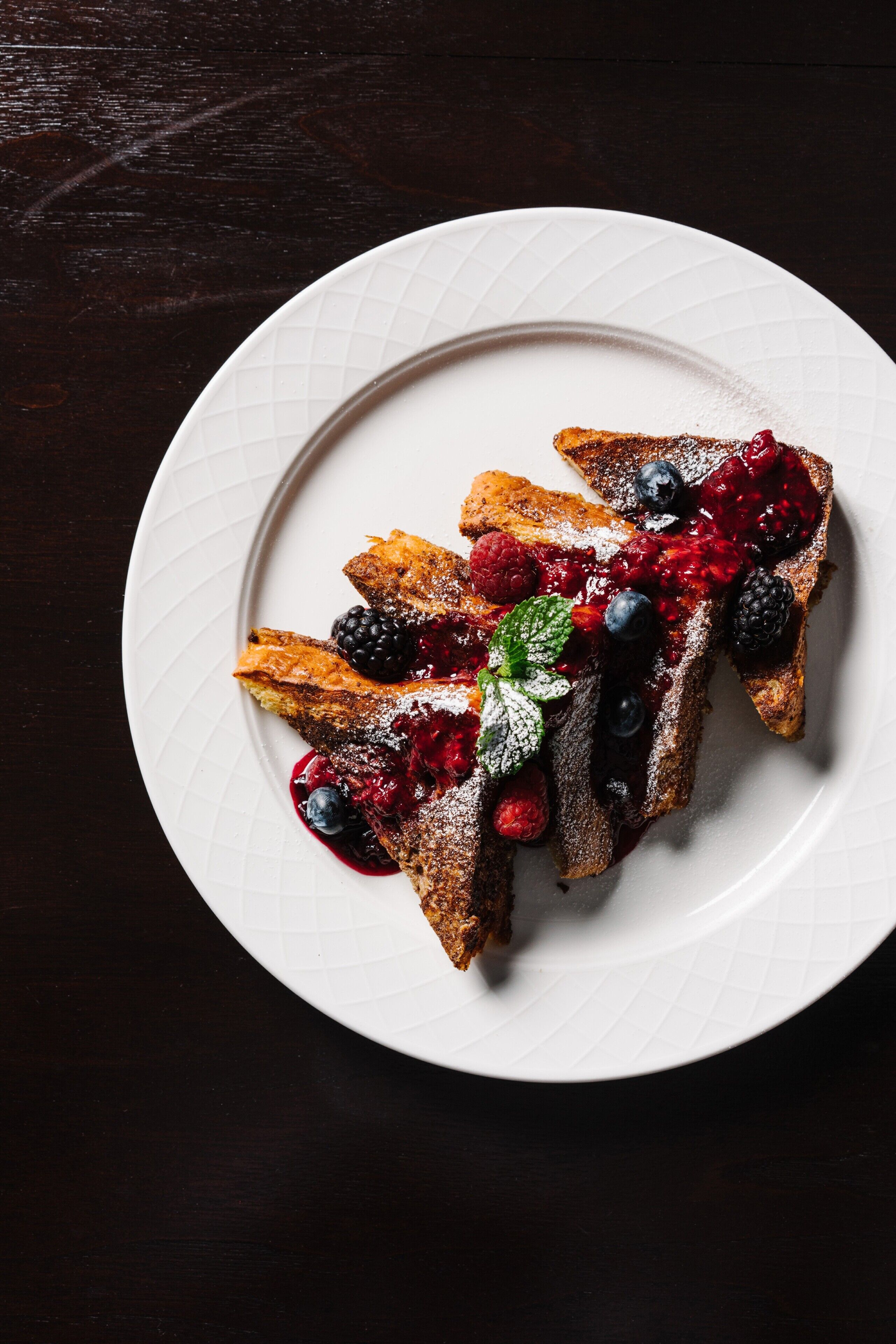 A white plate with French toast topped with berries and powdered sugar.