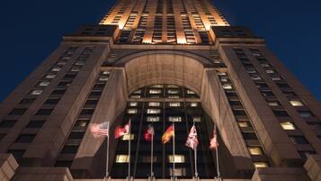A tall building with a prominent entrance featuring a large arched doorway and multiple flags.
