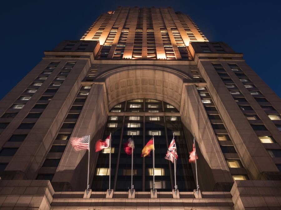 A tall building with a prominent entrance featuring a large arched doorway and multiple flags.
