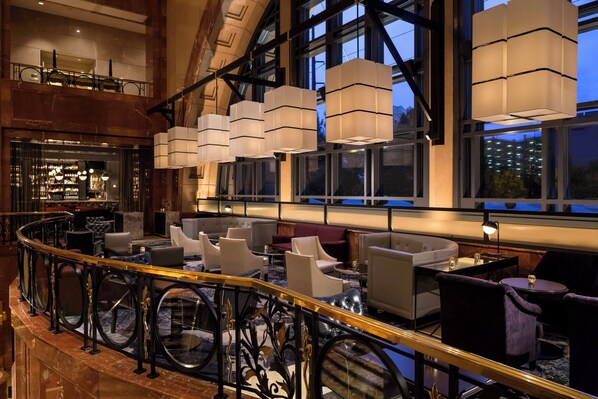 A spacious lobby with a marble floor, a curved black railing, and multiple seating areas with modern furniture.