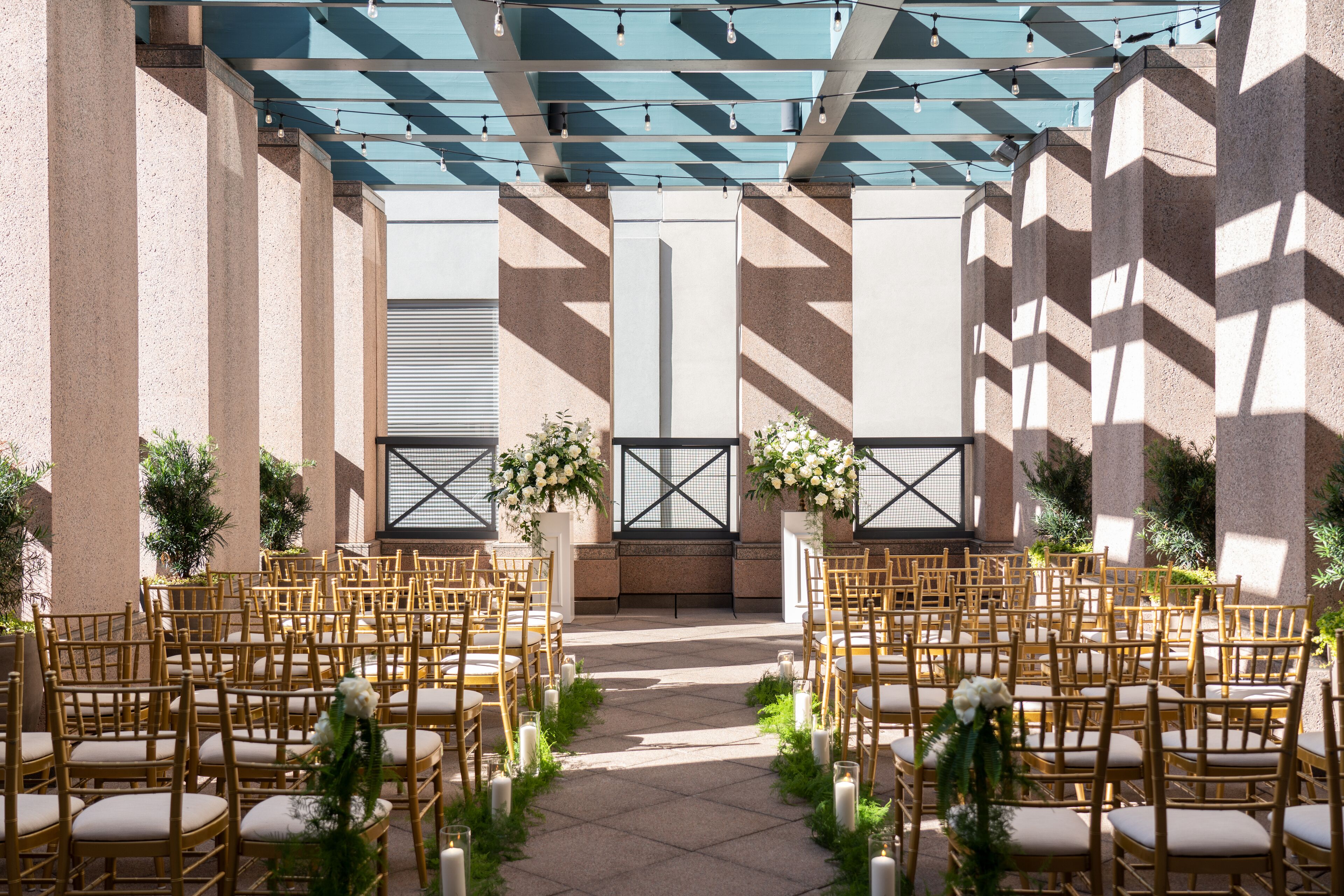 An outdoor wedding venue with rows of wooden chairs, a central aisle, and floral arrangements.