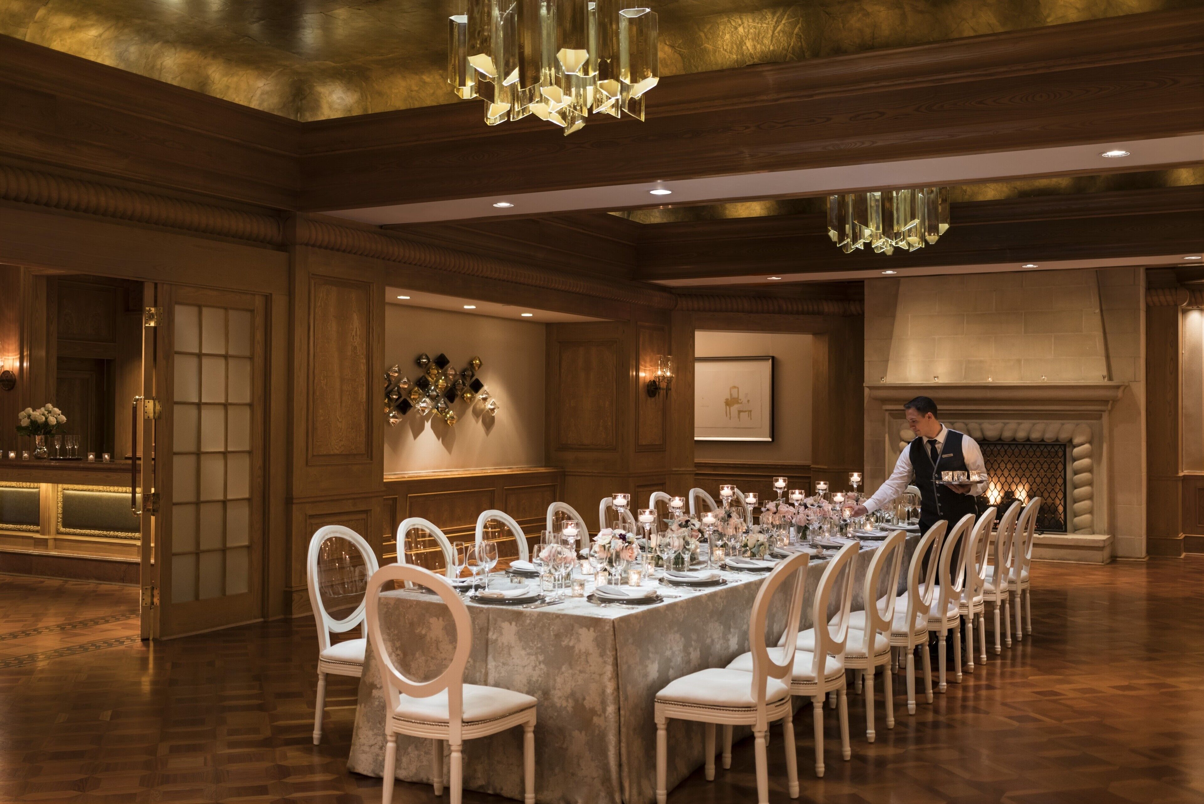Uma sala de jantar formal com uma longa mesa posta para refeição, painéis de madeira e um lustre.