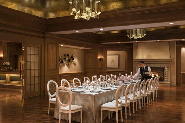 A formal dining room with a long table set for a meal, wooden paneling, and a chandelier.
