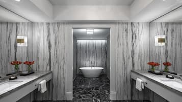 A modern bathroom with marble walls, a central bathtub, and two sinks with red flowers.