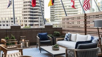 A rooftop terrace with a seating area, including a sofa and chairs, a coffee table, and a small plant.