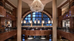 A grand lobby with a high ceiling, large chandeliers, and a central staircase.