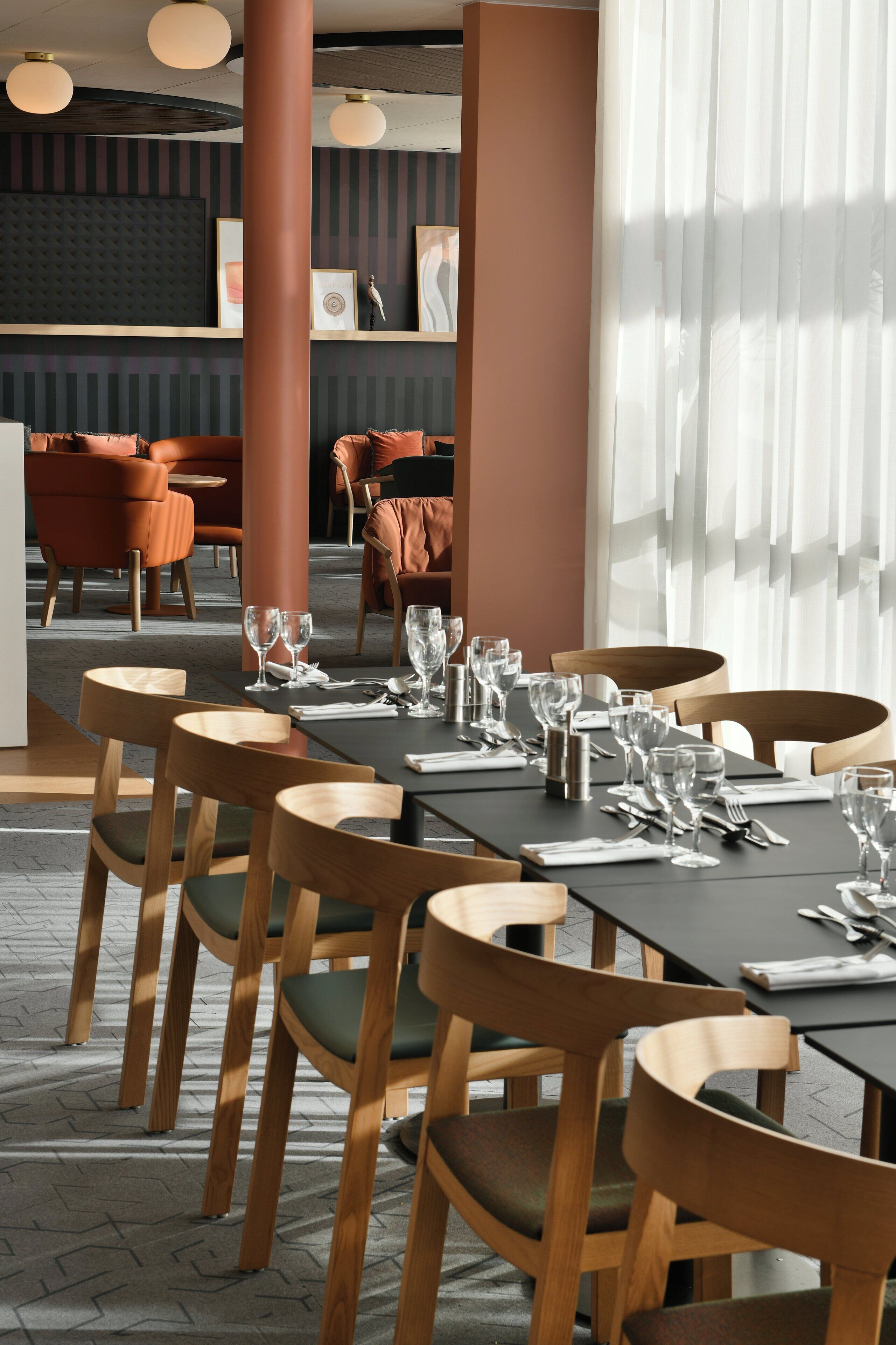 Interior de restaurante con sillas y mesas de madera, un área de bar al fondo y un ventanal con persianas.