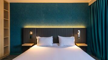 Una cama grande con ropa de cama blanca, dos mesitas de noche y una lámpara fijada a la pared.