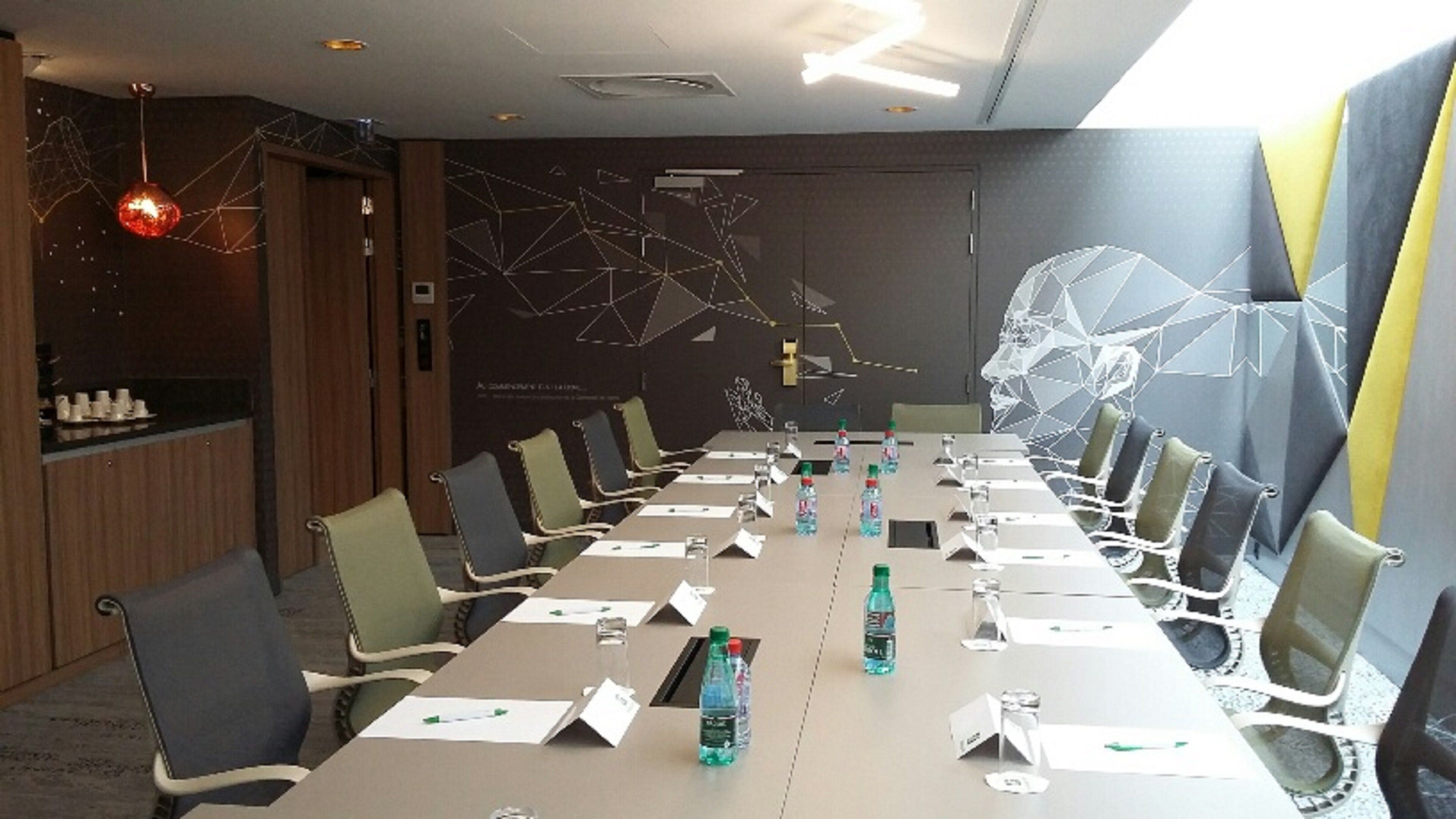 A conference room with a long table, chairs, name cards, water bottles, and a decorative light fixture.