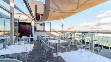 An outdoor dining area with tables and chairs, overlooking a cityscape.