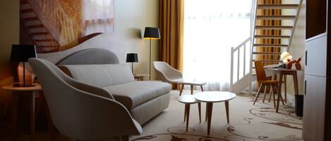 A hotel room with a sofa, two chairs, a small table, a lamp, and a staircase.