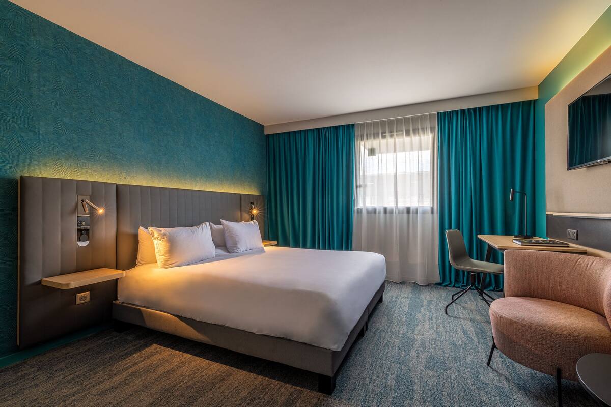 A hotel room with a large bed, a desk, a chair, and a TV.