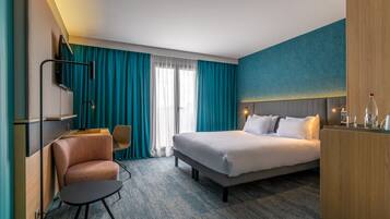 A hotel room with a bed, a desk, a chair, and a TV.
