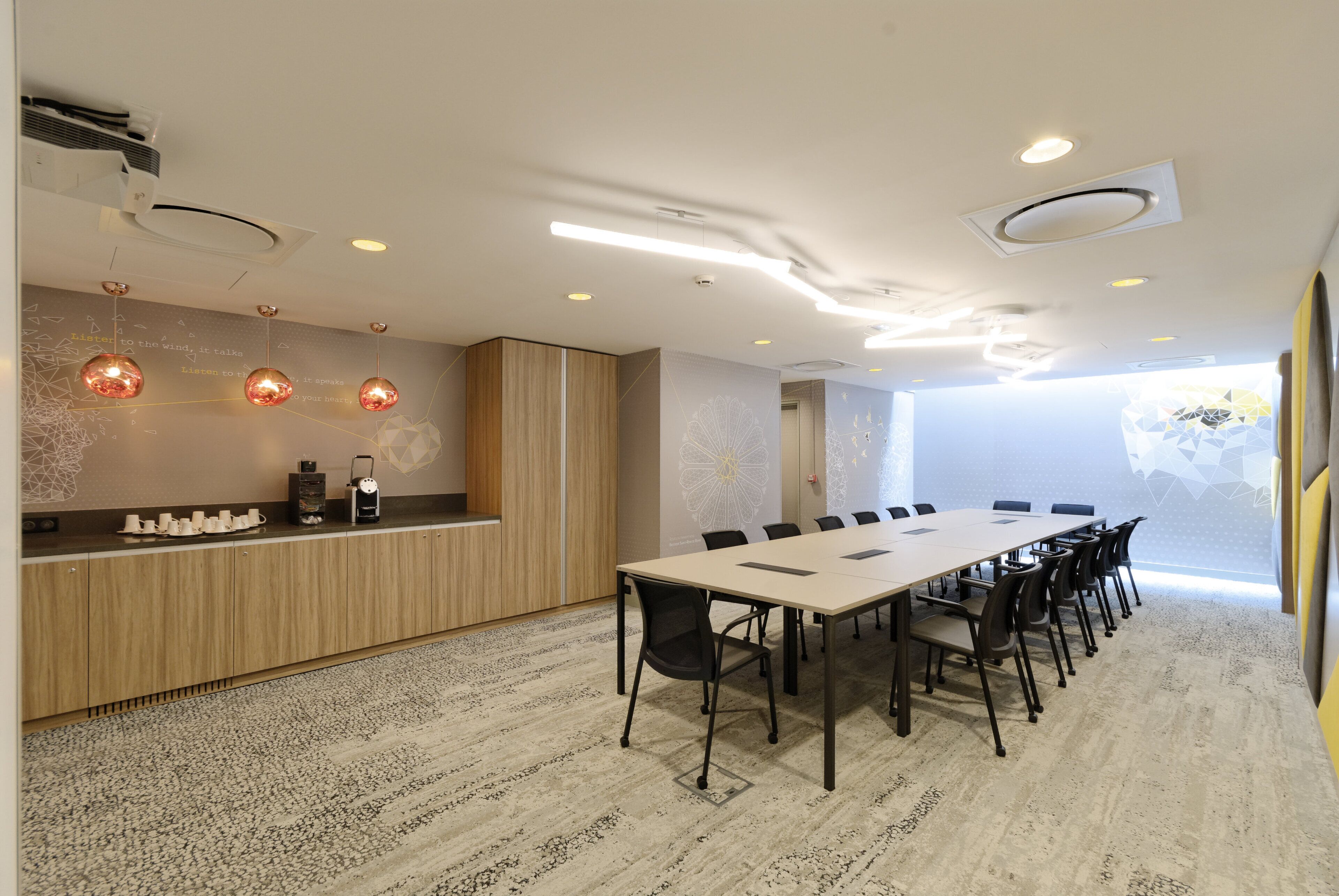 A modern meeting room with a long table, chairs, a coffee station, and a decorative wall.