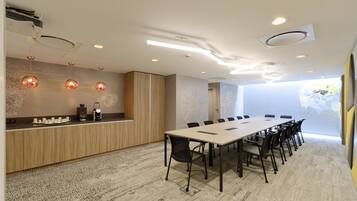 A modern meeting room with a long table, chairs, a coffee station, and a decorative wall.