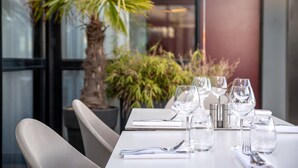 A dining table set with glasses, cutlery, and a menu, with a palm tree and plants in the background.