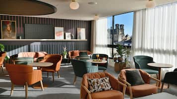 A modern lounge area with comfortable seating, a bar area, and large windows offering city views.