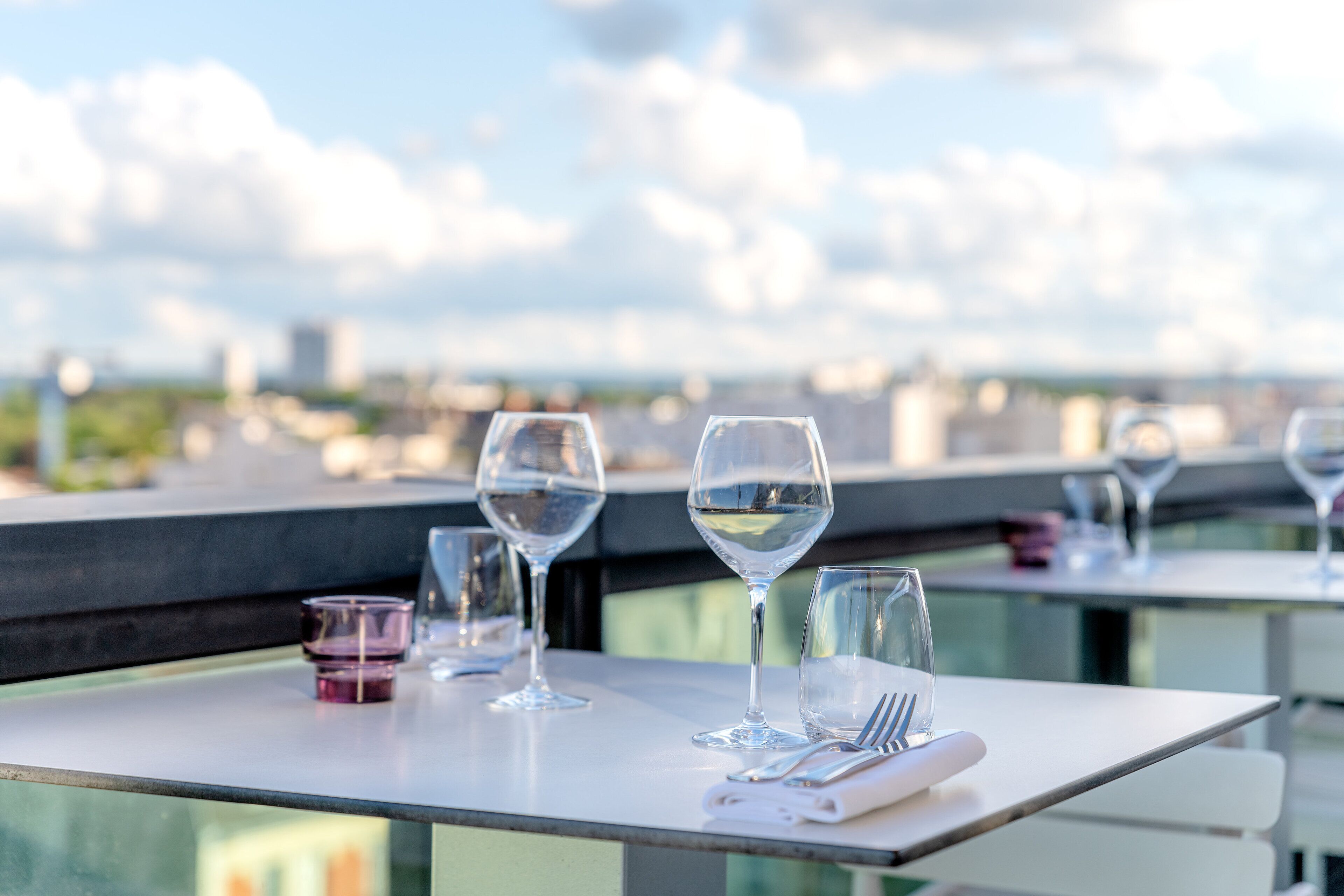 Une table à manger, avec des verres à vin et des couverts, donnant sur un paysage urbain.